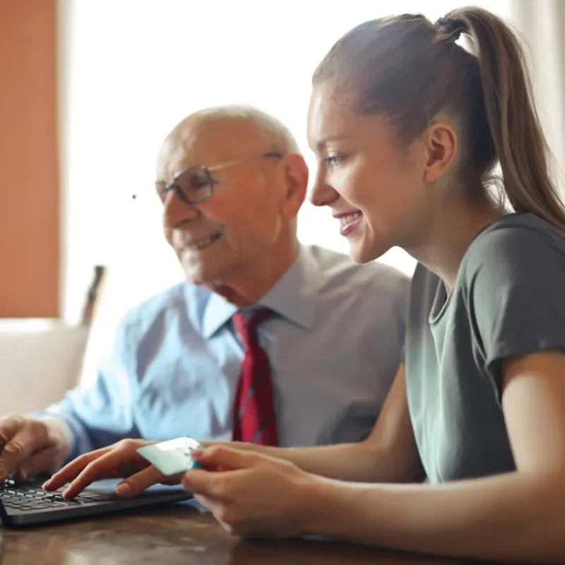 A woman and an elderly gentleman sitting down at a Laptop.