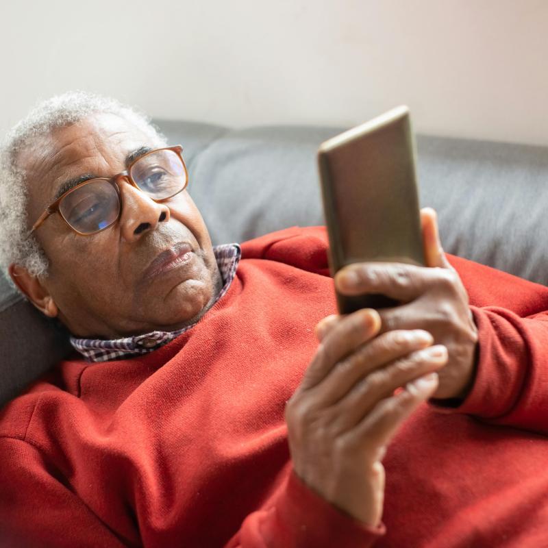 An elderly man with glasses using a mobile phone.