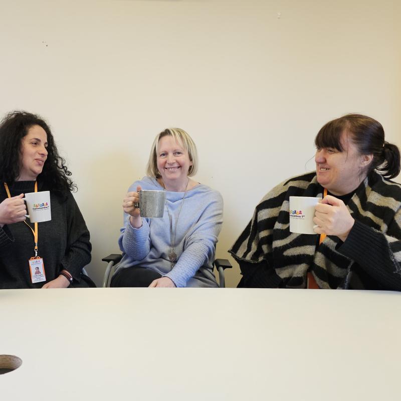 Three members of Communities 1st staff with hot drinks and smiles.