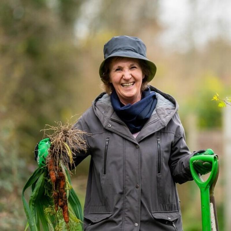 Woman wearing winter coat and hat, smiling while gardening. Image credit: David Tett