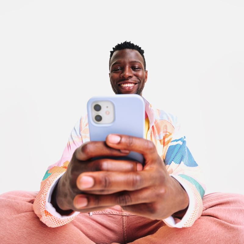 Man wearing pink and blue, smiling at his lavender phone. 