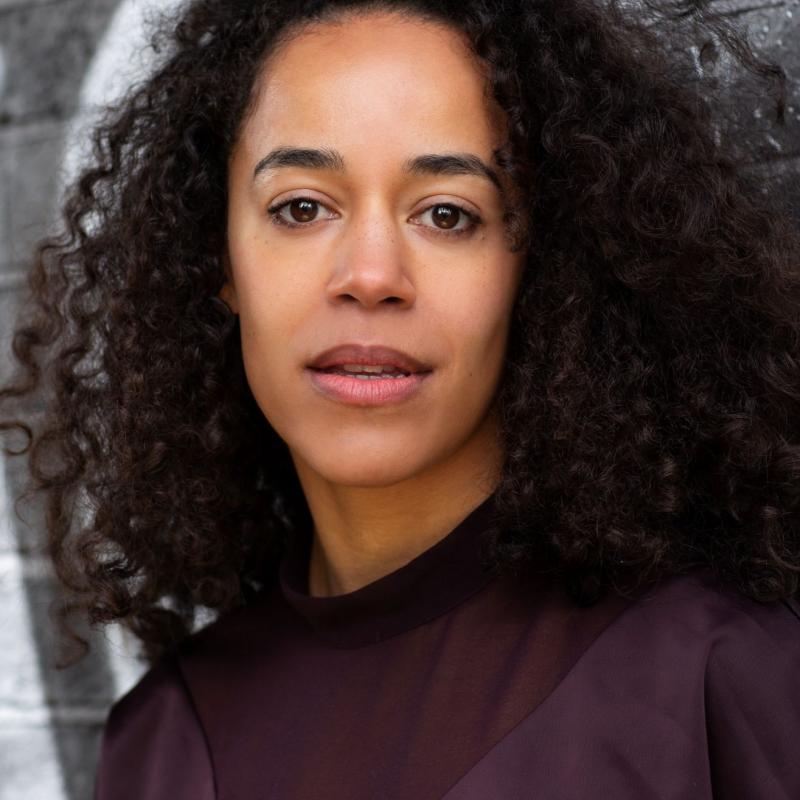 headshot of Communities1st Creative Producer Leda Douglas, a woman with curly hair wearing a purple shirt.